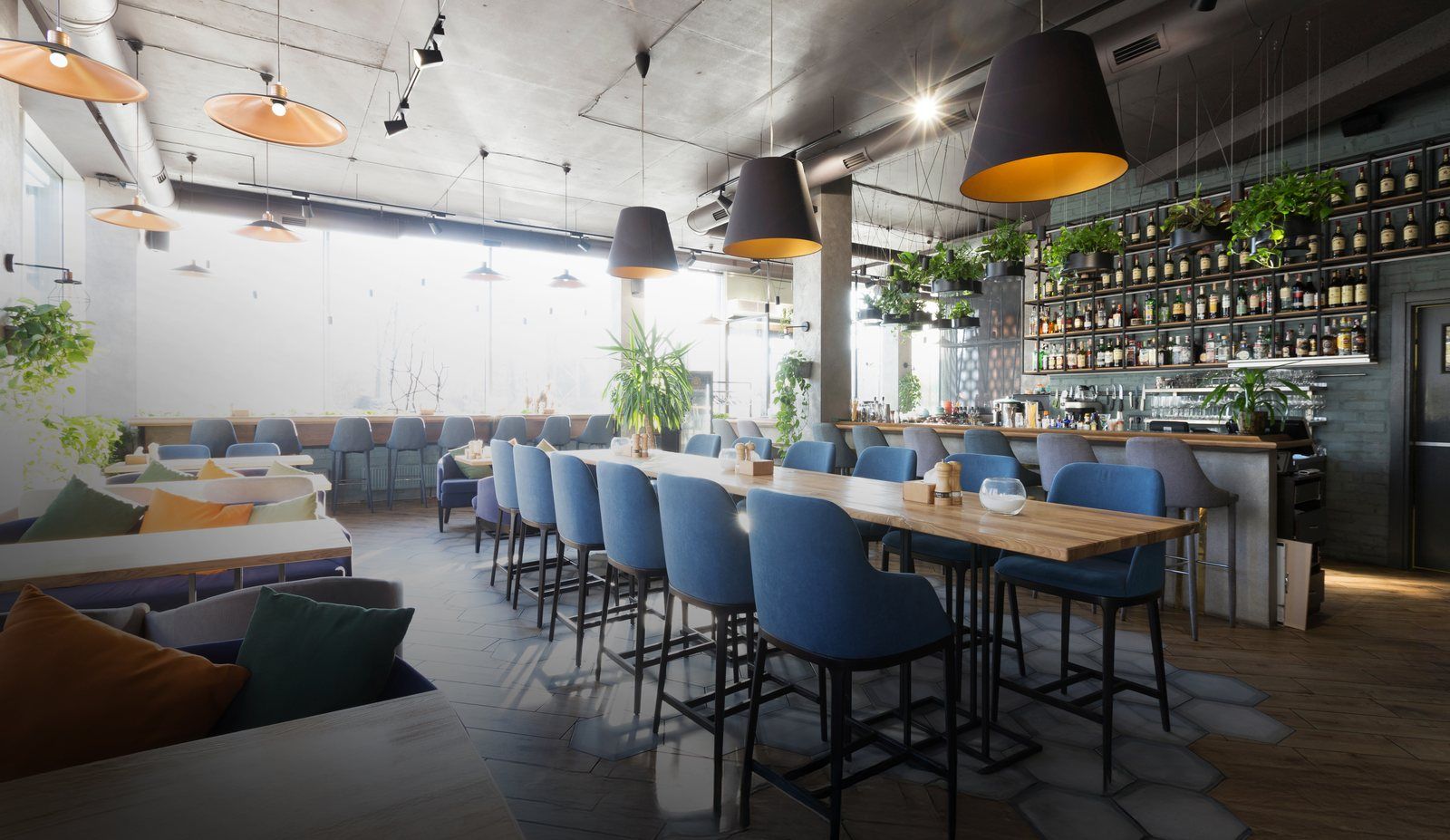 Salle de restaurant lumineuse : longue table haute bordée de chaises bleues, bar et suspensions