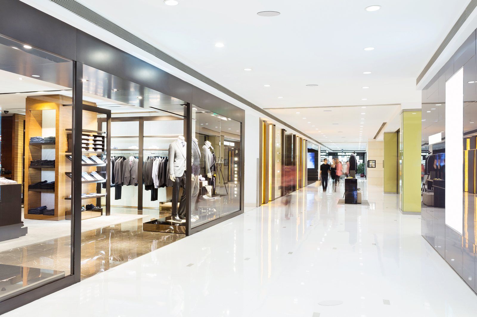 Allée de galerie commerciale bordée de boutiques de mode, plafond équipé d'enceintes encastrées